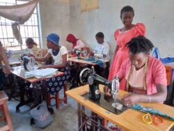 A class of tailoring students sat at their sewing machines